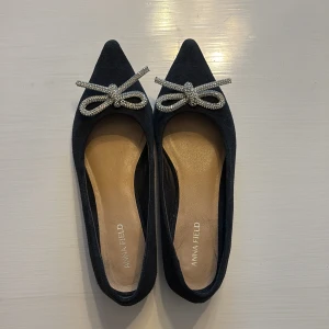 Svarta ballerinaskor med rosett Anna Field - Snygga svarta ballerinaskor från Anna Field med spetsig tå och glittrig rosettdetalj framtill. Skorna är gjorda i mocka och har en platt sula för skön komfort. Perfekt för dig som gillar stilrena och glamorösa detaljer. Nypris ca 800kr 