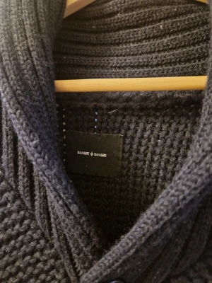 Mörkblå stickad kofta från Samsøe Samsøe - Säljer en mörkblå, grovstickad kofta från Samsøe Samsøe med bred krage och stora ribbade fickor. Koftan har knappar framtill och långärmade ärmar. Perfekt för dig som gillar chill och stilren look.