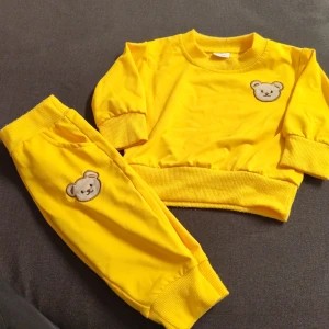 Gul sweatshirt med björn för baby - Superfin gul sweatshirt för baby med långärmade muddar och gulligt björnansikte broderat på bröstet. Tröjan har ribbade detaljer vid hals, ärmslut och nederkant. Perfekt för små som gillar färg och söta motiv.