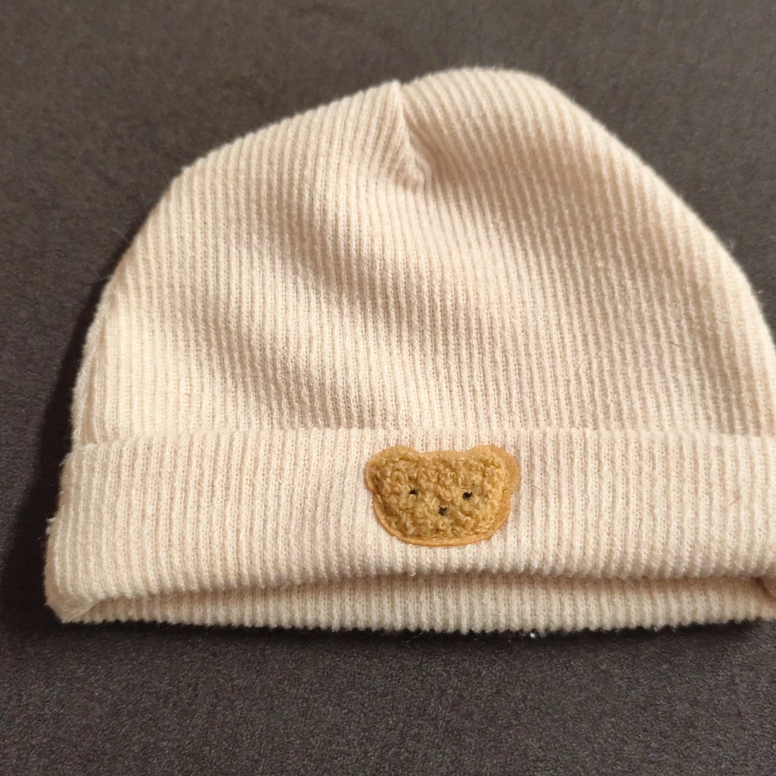 Beige ribbad mössa med nalledekor