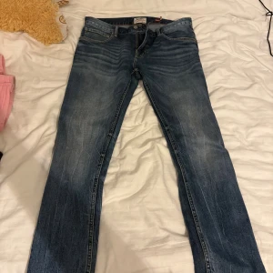 Blå Replay Anbass jeans - Säljer ett par blå Replay Anbass jeans med snyggt slitna detaljer och klassisk femficksdesign. Jeansen har en smal passform och är tillverkade i mjukt denimtyg som sitter skönt hela dagen. Perfekta för dig som gillar en modern och stilren look.