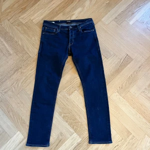 Jack & Jones Slim Glenn jeans blå 32/30 - Mörkblå jeans från Jack & Jones, modell Slim Glenn. Klassisk femficksdesign, slim fit och raka ben. Snygga kontrastsömmar och normal midja. Perfekta för dig som gillar en smalare passform och stilren look. Hör av er vid frågor