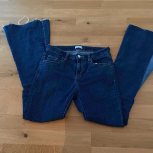 Blå bootcut jeans - Säljer ett par blå jeans med bootcut, fransig kant längst ner. Jeansen har en cool infälld ljusare jeanskil på insidan av benen som ger extra vidd och retro vibe. Klassisk femficksmodell och midja med knapp och dragkedja.