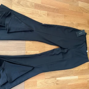 Svarta bootcut-byxor från Zara - Snygga svarta bootcut-byxor från Zara med markerad pressveck och breda ben. Byxorna har hög midja och coola slitsdetaljer vid bensluten som ger extra edge. Materialet är mjukt och har en lätt stretch för skön passform.