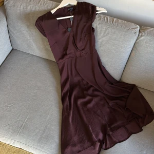 Mörkbrun klänning från Stockh LM - Säljer en elegant mörkbrun klänning från Stockh LM med v-ringning och korta ärmar. Klänningen har en mjuk, flowy siluett och stängs med dragkedja i ryggen. Materialet är slätt och har ett fint fall, perfekt för dig som gillar stilrena plagg med lite extra edge. Fastsydd underkjol. Lite shine i tyget. Aldrig använd. Prislapp på. 