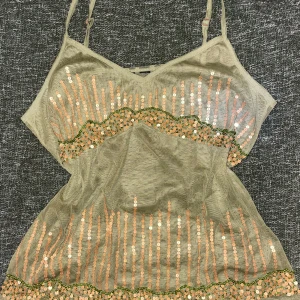 Olivgrön linnr med paljetter - Säljer en olivgrön linnetopp med smala axelband och guldiga paljetter. Säljer då den inte kommer till användning. Storlek runt M