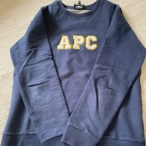 Mörkblå sweatshirt från A.P.C. - Snygg mörkblå sweatshirt från A.P.C. med broderad vit och gul logga på bröstet. Perfekt för dig som gillar stilrena college-vibbar och fransk design.