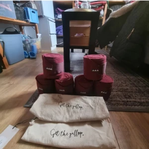 Vinröda stallbandage Get the Gallop - Säljer två set med vinröda benlindor från Get the Gallop. Benlinderna är i mjukt syntetmaterial och kommer i praktiska tygpåsar med tryck. Perfekta för ridning och skydd av hästens ben i stallet. Aldrig använda, vunnit på tävling och låtit stå i sadelkammaren därför påsarna är lite smutsiga🩷