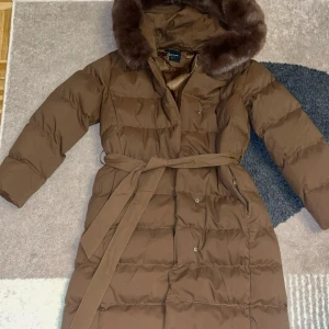 Brun lång vinterjacka  - PRIS KAN DISKUTERAS VID SNABB OCH SERIÖS AFFÄR! Snygg brun pufferjacka från Copperose med fluffig fuskpäls runt huvan och bälte i midjan. Jackan är lång, har knappar och dragkedja framtill samt två fickor. Perfekt för kalla dagar och har en riktigt elegant look. Denna jackan är väldig till jackor från furstockholm osv. Den är inte min stil längre därav vill jag sälja den. Den är som helt ny, använt endast 1 gång förra året och har ej använt den sen dess. Den är jättetjock och pälsen är äkta.