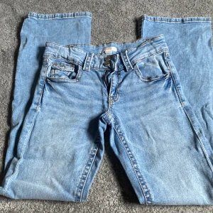 Blå jeans från Gina Tricot, storlek 164 - Snygga ljusblå jeans från Gina Tricot i klassisk femficksmodell med raka ben och dubbla knappar i midjan. Jeansen har kontrastsömmar och är tillverkade i slitstarkt bomullsjeansmaterial. Perfekt för dig som gillar enkel och tidlös stil.