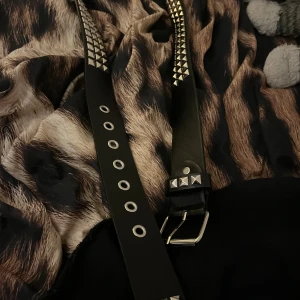 Svart nitarbälte - Säljer ett svart bälte med silvriga fyrkantiga nitar och metallspänne. Bältet har flera hål med metallringar. Perfekt accessoar för att ge outfiten en edgy vibe. Aldrig använd