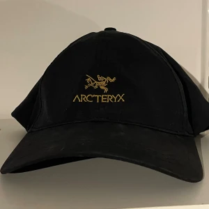 Svart keps från Arc'teryx - Svart keps från Arc'teryx med gul broderad logga framtill. Klassisk böjd skärm och justerbar passform. 