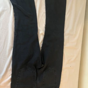 Svarta bootcut jeans med fem fickor - Säljer ett par svarta jeans med klassisk femficksdesign och bootcut-ben. Jeansen har en mörk tvätt och är tillverkade i jeansmaterial med dragkedja och knapp framtill. Perfekta för dig som gillar en lite vidare passform nedtill.