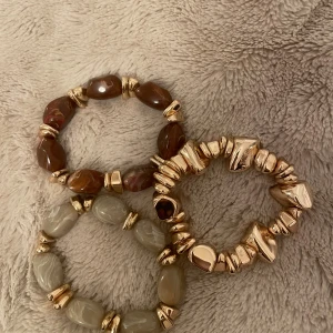 Tre chunky armband med stenar och guld - Säljer ett set med tre chunky armband. Ett med bruna stenar och guldfärgade detaljer, ett med beige stenar och guldfärgade pärlor, och ett helt i oregelbundna guldfärgade pärlor. Perfekt för dig som gillar statement-smycken och att mixa olika färger och former.