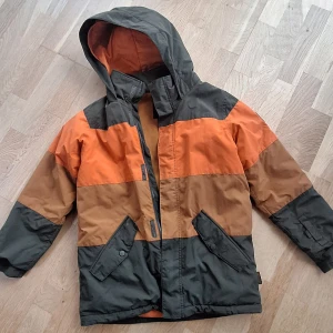 Burton vinterjacka med huva - Symbol Jacket är en mångsidig jacka med tuff design. Den fungerar både i backen och på skolgården. Vattentätt och tejpade sömmar på utsatta ställen håller dig både torr och varm. Hjälmkompatibel huva, ventilation under armarna och snökjol. Jackan har även en smart liftkortsficka, goggleficka samt handvärmarfickor med dragkedja. En tuff jacka för dig som vill synas len också ställer krav på funktion.