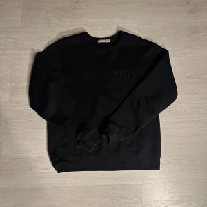 Svart sweatshirt från Tiger of Sweden - Svart sweatshirt från Tiger of Sweden med diskret logotyp broderad på bröstet. Tröjan har rund hals, långa ärmar och ribbade muddar vid ärmslut och nederkant. Perfekt för en clean och stilren look.