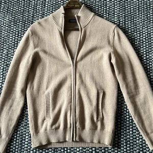 Brun stickad kofta från Dressmann - Säljer en brun stickad kofta från Dressmann med dragkedja och ribbade detaljer vid krage och ärmslut. Perfekt för kyligare dagar. Koftan har en klassisk design som passar till många tillfällen.