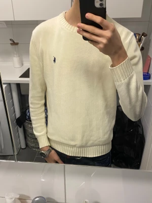 Creme Vit stickad tröja från Polo Ralph Lauren - Lägg gärna pris förslag. Creme Vit stickad tröja från Polo Ralph Lauren med klassisk rund hals och ribbade muddar. Tröjan har en broderad marinblå logga på bröstet och är långärmad. Perfekt för dig som gillar clean och stilren look.