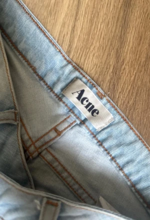 Ljusblå raka jeans från Acne - Säljer ett par ljusblå jeans från Acne med klassisk femficksdesign och raka ben. Jeansen har snygga slitningar och kontrastsömmar, tillverkade i bomullsdenim. Perfekta för dig som gillar en clean och stilren look.