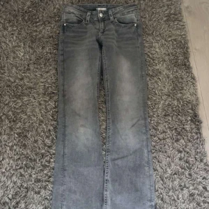 Grå bootcut jeans från Gina Tricot - Snygga grå jeans från Gina Tricot i bootcut-modell. Jeansen har klassisk femficksdesign, knäppning med dragkedja och knapp samt coola bakfickor med knappdetalj. Perfekta för dig som gillar en avslappnad men trendig look.