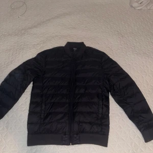 Svart dunjacka Super Light Down M - Svart dunjacka från Super Light Down i storlek M. Jackan har quiltad design, ribbad krage och muddar samt dragkedja framtill. Lätt och smidig modell som passar perfekt när du vill ha en stilren look och samtidigt hålla dig varm.