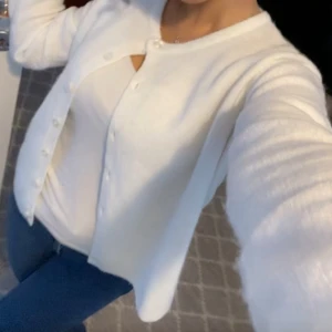 Vit stickad kofta lager 157 - Supermjuk och stilren vit stickad kofta med rund hals och knäppning framtill. Långärmad modell som är perfekt att slänga över en topp eller t-shirt. Storlek 150 men passar xs/s beroende på hur man vill att den ska sitta. 