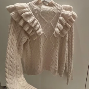 Stickad tröja - Beige stickad tröja från ONLY i storlek S med breda volanger över axlarna och kabelstickat mönster. Hög hals och långa ärmar med ribbade muddar. Perfekt för vintern. Skriv för mer info💕