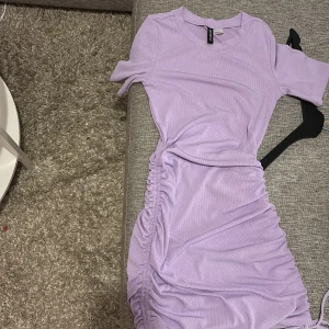 Ljuslila ribbad kortklänning H&M Divided - Supersöt ljuslila kortklänning från H&M Divided i ribbad bomull. Klänningen har korta ärmar och snygga rynkade detaljer med snörning längs sidorna som ger en cool och trendig look. Perfekt för dig som gillar färg och vill sticka ut lite extra.