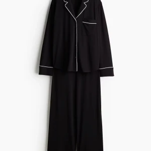 Svart pyjamas  - Mjuk och skön svart pyjamas från Lindex i storlek S. Setet består av långärmad skjorta med vit piping längs krage, ärmslut och ficka samt matchande byxor med vit kant. Klassisk och chill look, perfekt för hemmakvällar.