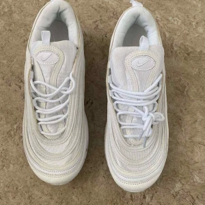 Nike Air Max 97 Triple White - Säljer ett par Nike Air Max 97 i helvitt. Skorna har den ikoniska vågiga designen, synlig Air Max-sula och snörning. Ovandelen är i mesh och syntet med broderad Swoosh på sidan och tungan. Perfekta för dig som gillar en clean och sportig look.