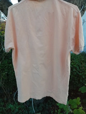 Beige pikétröja från Polo Ralph Lauren - Snygg beige pikétröja från Polo Ralph Lauren med klassisk krage och blå ränder. Tröjan har korta ärmar, knappslå och en bröstficka med blå broderad logga. Tillverkad i mjuk bomull som är skön mot huden. Perfekt för dig som gillar stilren och enkel design.