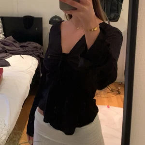 Svart omlottopp med knyt fram - Säljer en svart omlottopp med lång ärm och djup v-ringning. Toppen har en snygg knytning framtill som ger en trendig look. Perfekt att styla med kjol eller jeans för en cool outfit.