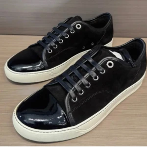 Svarta sneakers från Lanvin med lackad tå - Snygga svarta sneakers från Lanvin med vit platt sula och snörning. Ovandelen är i mocka och tån har en glansig lackad finish som ger en cool kontrast. Metallfärgade öljetter och klassisk rund form. Perfekt för dig som gillar stilrena och exklusiva sneakers.
