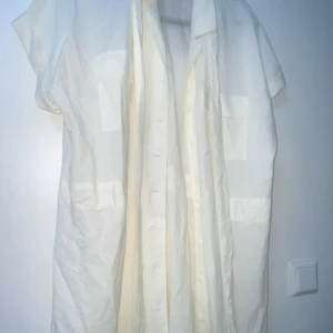 Vit skjortklänning från Bik Bok XL - Säljer en vit skjortklänning från Bik Bok i storlek XL. Klänningen har korta ärmar, knappar hela vägen framtill och flera fickor som ger en cool utility-vibe. Perfekt för dig som gillar en avslappnad och stilren look.