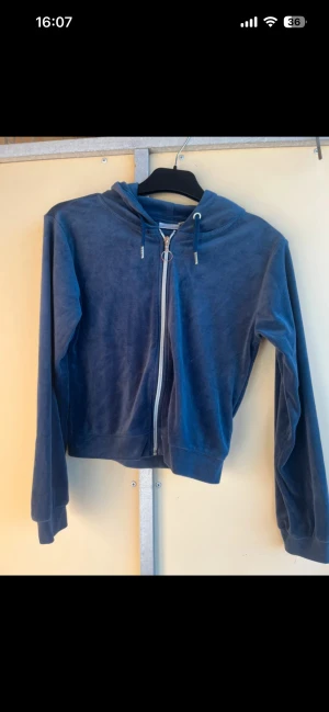 Blå velour hoodie med dragkedja - Mjuk och skön hoodie i mörkblå velour med huva och snörning. Tröjan har en hel dragkedja framtill och långa ärmar. Perfekt för chill dagar eller när du vill ha en avslappnad look. Från Gina storlek S