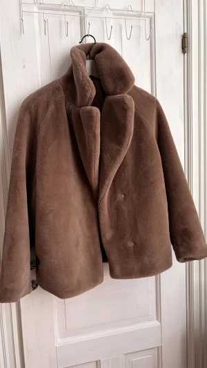 Brun teddyjacka från H&M XS - Säljer en brun teddyjacka från H&M i storlek XS. Jackan har en oversized krage, knäppning med dolda knappar och är tillverkad i mjukt syntetmaterial som ger en fluffig och mysig känsla. Perfekt för dig som gillar chill och comfy stil.