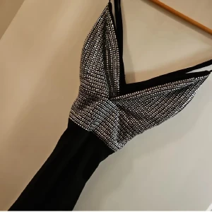 Svart kortklänning med glittrig topp - Svart kortklänning med en glittrig, silverfärgad topp i v-ringad modell och smala axelband. Överdelen har ett snyggt rutigt mönster av små silverprickar som ger en festlig vibe. Kjolen är enkel och stilren, vilket gör att toppen verkligen står ut.