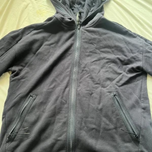 Svart hoodiejacka från C.P. Company - Svart hoodiejacka från C.P. Company med hel dragkedja, två fickor med dragkedja och ikoniska goggles i huvan. Jackan är i mjuk bomull och har lång ärm. Perfekt för dig som vill sticka ut med en unik streetwear-look. Skicket är nästintill helt nytt, kvitto finns och nypris ligger på runt 3200kr