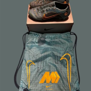 Nike Vapor 14 Elite FG fotbollsskor - Nike Vapor 14 Elite FG fotbollsskor i chlorine blue med laser orange detaljer. Snyggt rutigt mönster och orange swoosh på sidan. Skorna är tillverkade i Flyknit-material för grym passform och lätt känsla. Platt sula med dobbar för spel på naturgräs. Medföljer matchande dustbag.Skorna är i andhämtning skick!