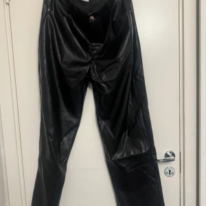 Svarta skinnbyxor med wide fit - Snygga svarta skinnbyxor med rak och bred passform. Byxorna har klassisk femficksdesign, knapp och dragkedja framtill. Materialet är glansigt syntetskinn som ger en cool vibe. Perfekta för dig som vill sticka ut med en edgy look.