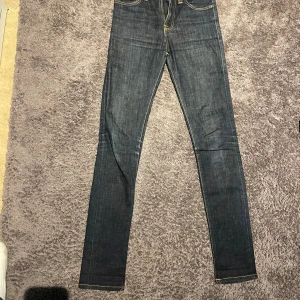 Mörkblå jeans från Nudie Jeans - Snygga mörkblå jeans från Nudie Jeans i storlek 27/32. Klassisk femficksmodell med kontrastfärgade sömmar. Jeansen är tillverkade i slitstarkt denim och har en tidlös look som funkar till allt.