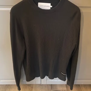 Svart stickad tröja Calvin Klein Jeans - Svart stickad tröja från Calvin Klein Jeans i kashmirblandning. Tröjan har ribbad struktur framtill, rund halsringning och diskret logga nertill. Perfekt för dig som gillar stilrena och klassiska plagg med en modern touch.