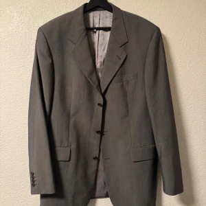 Grå kavaj från Hugo Boss i ull/mohair - Snygg grå kavaj från Hugo Boss med klassisk passform. Tillverkad i exklusiv ull och mohair från Vitale Barberis Canonico. Kavajen har tre knappar framtill, två fickor med lock och en bröstficka. Fodret är silkeslent och grått för en lyxig känsla.