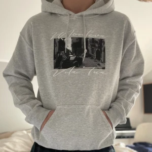 Montéva limited edition hoodie - Snygg ljusgrå hoodie från Monteva med svartvitt foto-tryck och texten 'Vita Tua' på bröstet. Deras limiterade kollektion. Tröjan har huva med snörning och en stor magficka. Perfekt för dig som gillar streetstyle och vill ha en chill look.