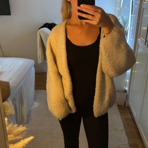 Beige stickad kofta från Lindex - Mysig och oversized beige stickad kofta från Lindex i storlek M/L. Koftan har långärmade, lite puffiga ärmar och är öppen framtill utan knappar. Perfekt att slänga på sig när det är lite kyligt och du vill ha en chill och comfy vibe.