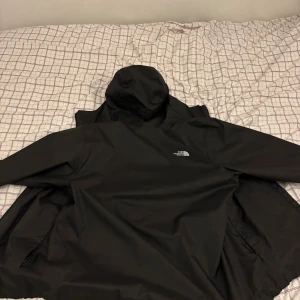 Svart regnjacka från The North Face - Svart regnjacka från The North Face med huva och dragkedja framtill. Säljer den för att den är för stor på mig. Men annars jackan är helt ny från Zolando. Mer info skriv till mig!