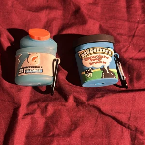 AirPods fodral Gatorade & Ben & Jerry's - Två roliga AirPods-fodral i silikon, formade som Gatorade-flaska och Ben & Jerry's glassbägare. Passar AirPods och har karbinhake för enkel fastsättning. Fodralen är i gott skick utan synligt slitage, perfekta för att skydda och ge din AirPods en unik look.
