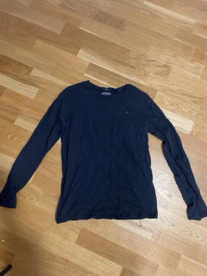 Mörkblå långärmad topp Tommy Hilfiger - Snygg mörkblå långärmad topp från Tommy Hilfiger i ekologisk bomull. Diskret logga broderad på bröstet och klassisk rund halsringning. Perfekt för dig som gillar stilrena och enkla plagg med en touch av premiumkänsla.