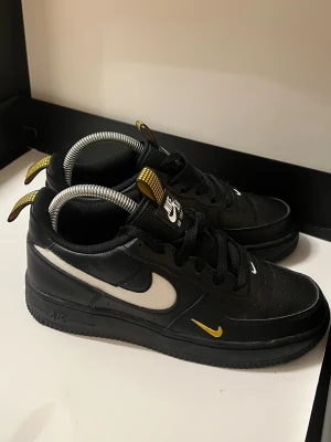 Nike Air Force 1 svart/gul sneakers - Nike Air Force 1 sneakers i svart skinn med vita och gula detaljer. Limited edition.  OBS PRIS KAN DISKUTERAS