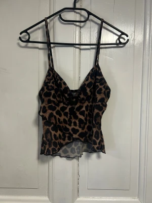 Leopardmönstrad linnetopp från SHEIN - Säljer en snygg leopardmönstrad linnetopp från SHEIN i storlek XS. Toppen har tunna justerbara axelband och är tillverkad i ett lätt och transparent polyestermaterial. Den har en v-ringad front och en croppad passform som ger en trendig look.